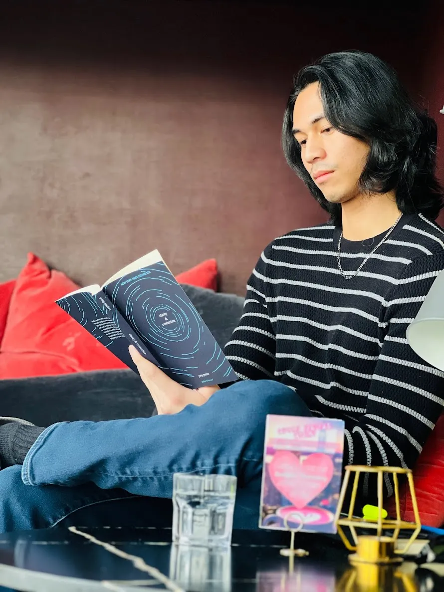 Person in a striped sweater sitting on a sofa reading a book titled 'Duality of Connection.'