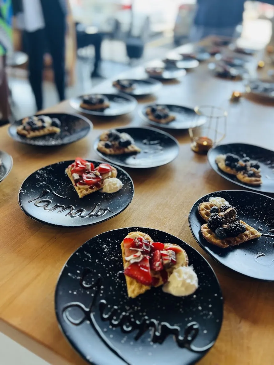 Heart-shaped waffles with strawberries or blueberries on black plates arranged on a wooden table.